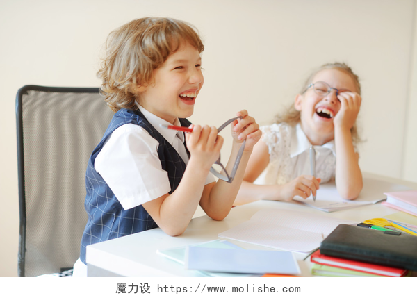 正在开心大笑的两个小孩有趣的学童，男孩和女孩，坐在一张桌子.